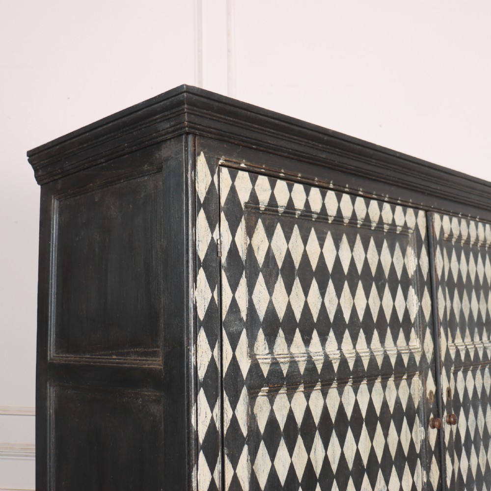 A tall English painted wooden linen cupboard featuring a black and cream harlequin diamond pattern across the front doors and drawers. View III
