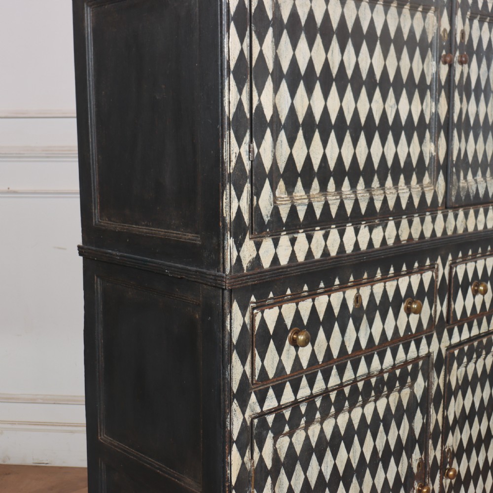 A tall English painted wooden linen cupboard featuring a black and cream harlequin diamond pattern across the front doors and drawers. View IV