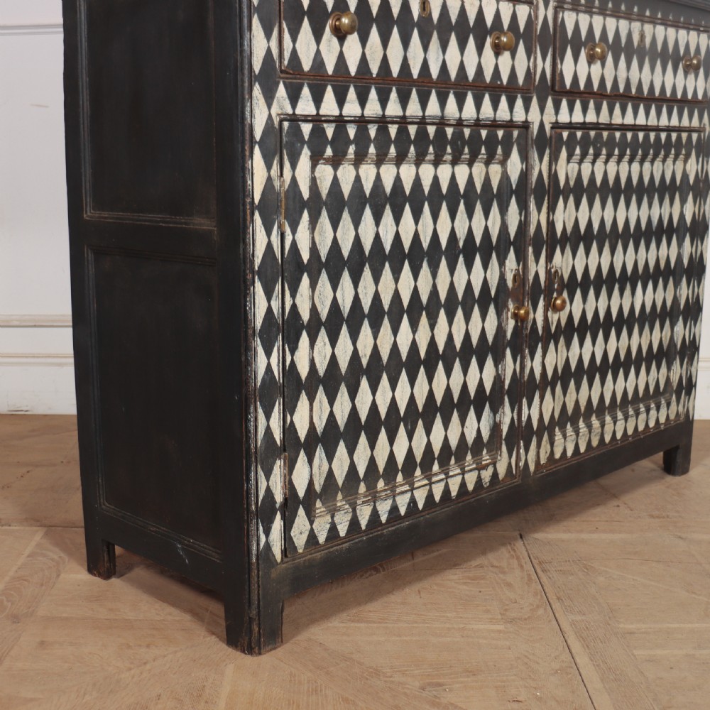 A tall English painted wooden linen cupboard featuring a black and cream harlequin diamond pattern across the front doors and drawers. View V