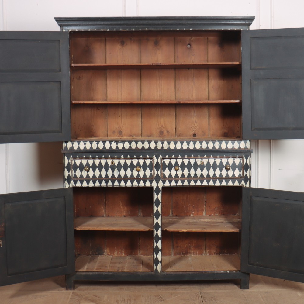 A tall English painted wooden linen cupboard featuring a black and cream harlequin diamond pattern across the front doors and drawers. View VI