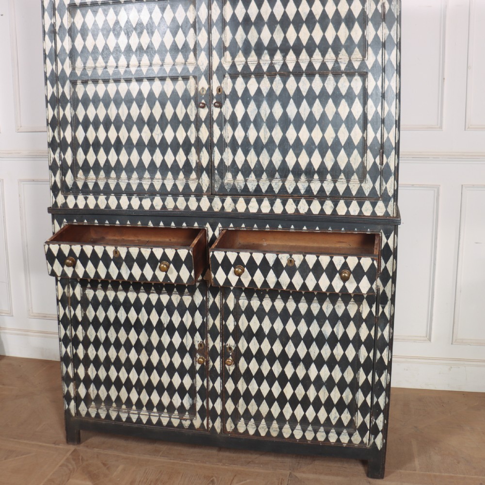 A tall English painted wooden linen cupboard featuring a black and cream harlequin diamond pattern across the front doors and drawers. View VII