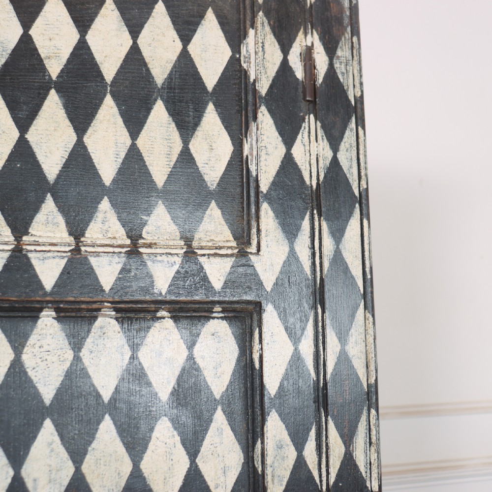A tall English painted wooden linen cupboard featuring a black and cream harlequin diamond pattern across the front doors and drawers. View VIII