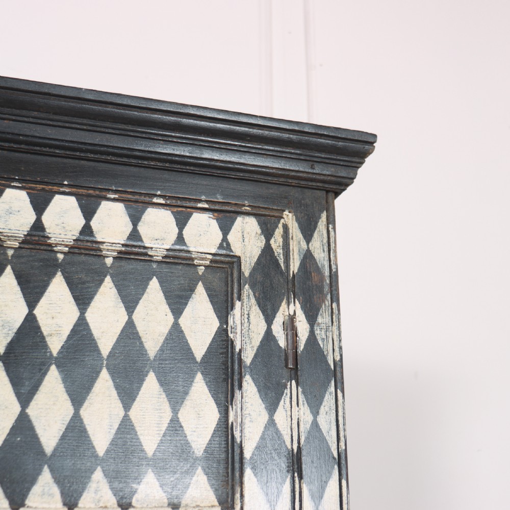 A tall English painted wooden linen cupboard featuring a black and cream harlequin diamond pattern across the front doors and drawers. View IX