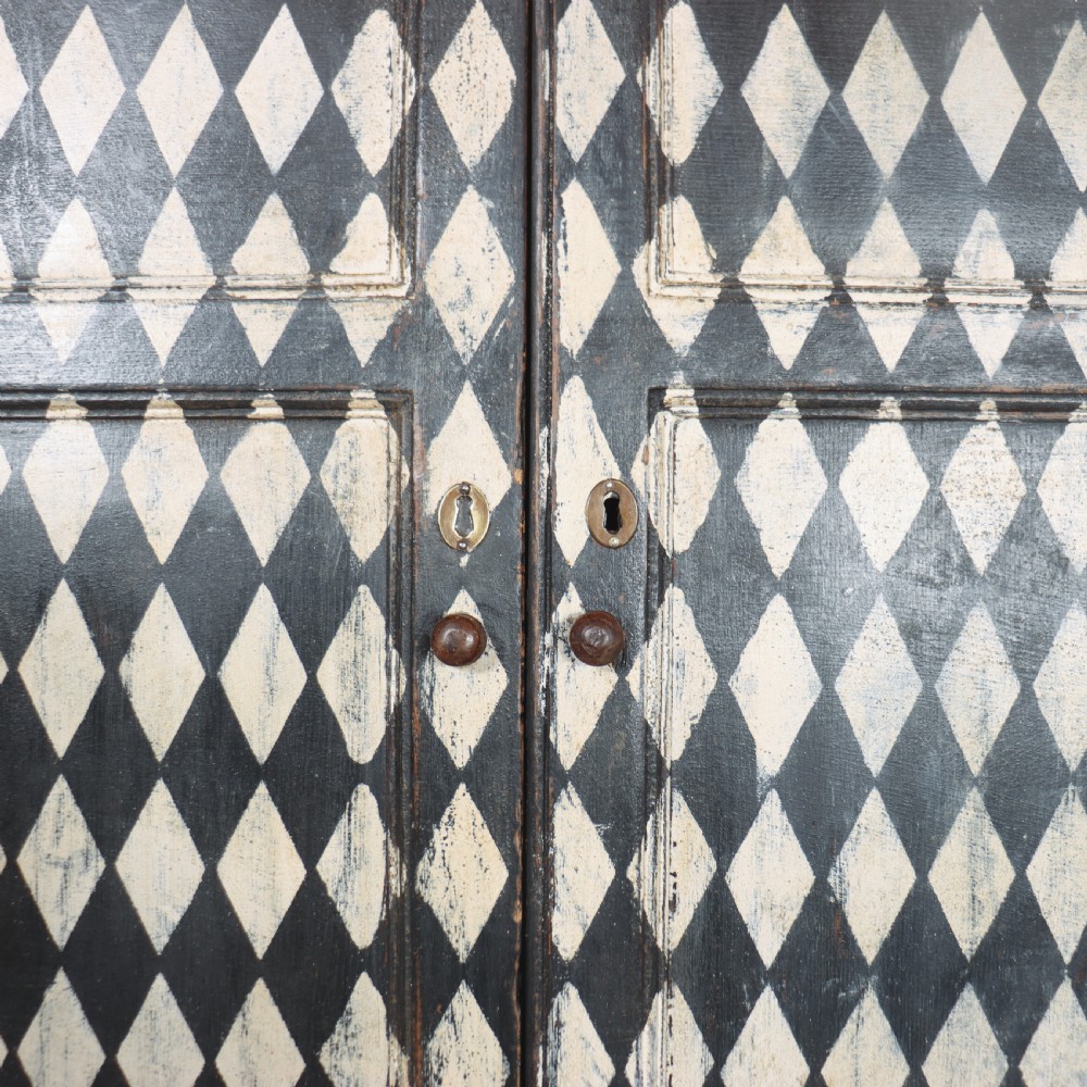 A tall English painted wooden linen cupboard featuring a black and cream harlequin diamond pattern across the front doors and drawers. View X