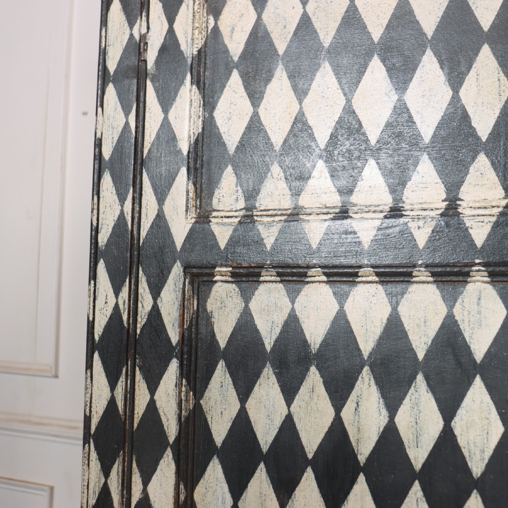 A tall English painted wooden linen cupboard featuring a black and cream harlequin diamond pattern across the front doors and drawers. View XI
