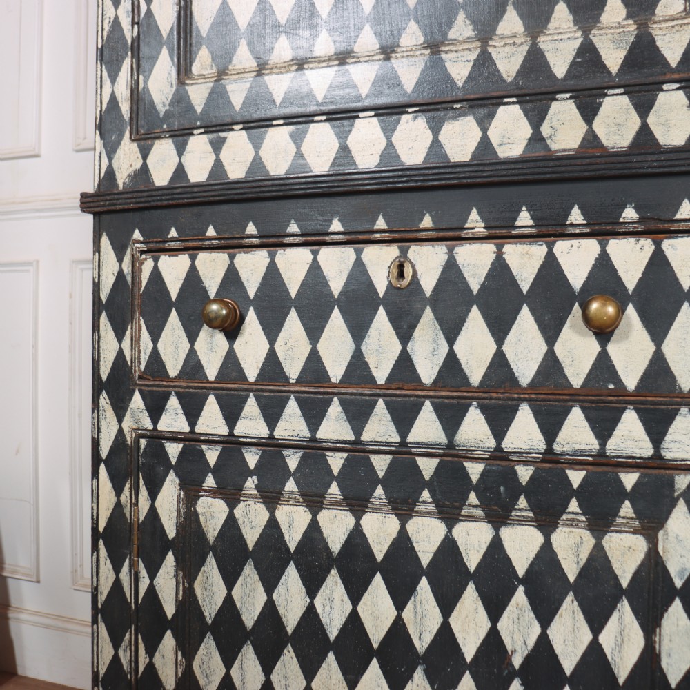 A tall English painted wooden linen cupboard featuring a black and cream harlequin diamond pattern across the front doors and drawers. View XII