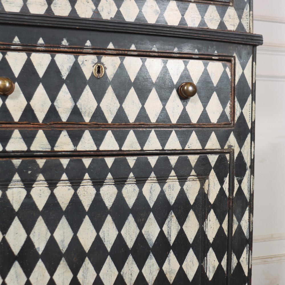 A tall English painted wooden linen cupboard featuring a black and cream harlequin diamond pattern across the front doors and drawers. View XIII