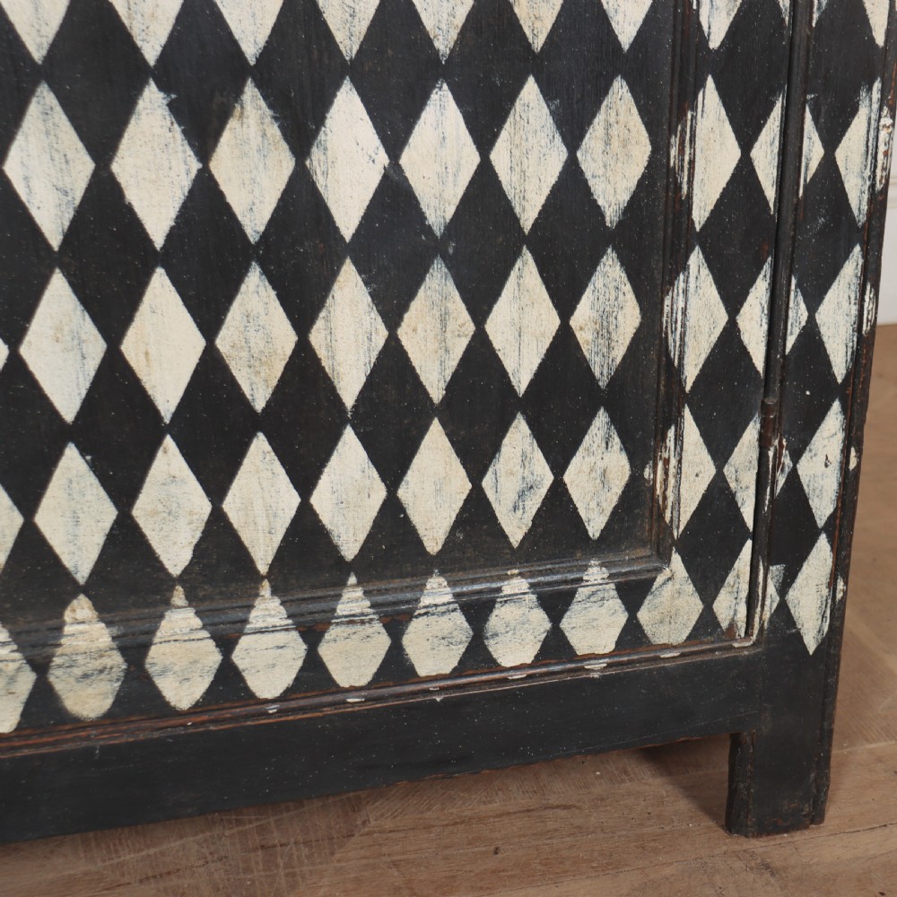 A tall English painted wooden linen cupboard featuring a black and cream harlequin diamond pattern across the front doors and drawers. View XIV