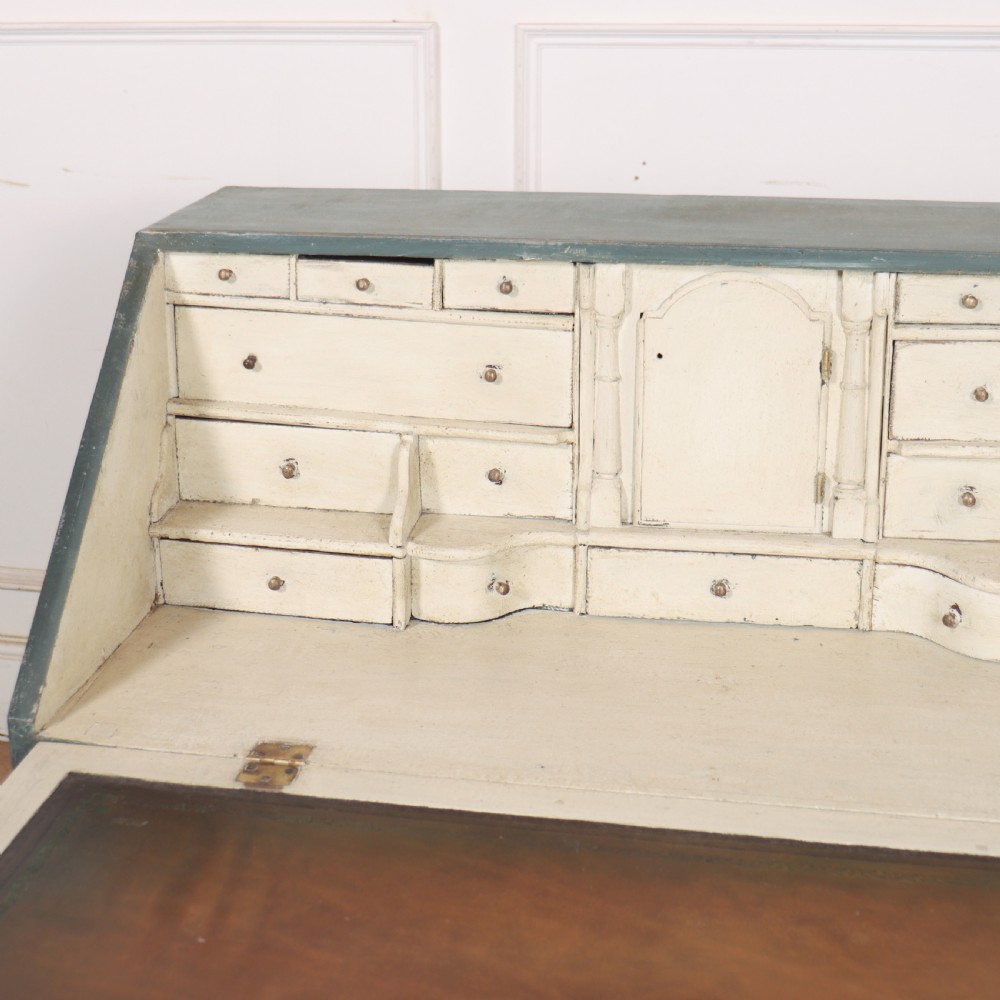 An 18th-century English slant-front bureau with a distressed grey-green painted finish, brass pull handles, and turned feet. View IV