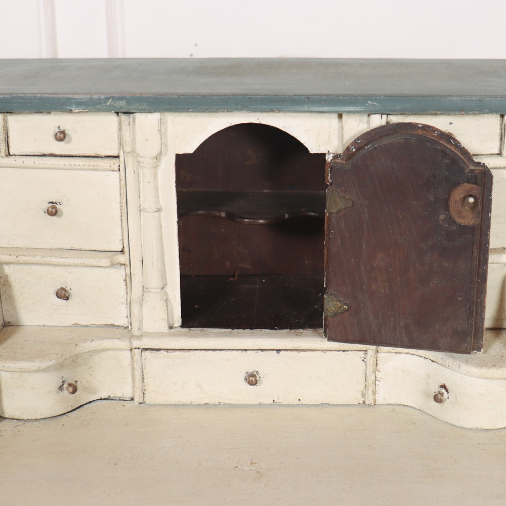 An 18th-century English slant-front bureau with a distressed grey-green painted finish, brass pull handles, and turned feet. View VI