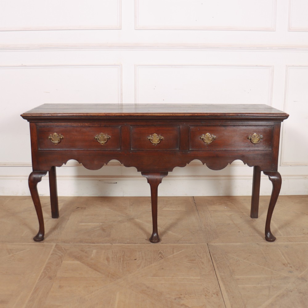 An 18th-century style dark oak dresser base featuring three frieze drawers, brass handles, a shaped apron, and elegant cabriole legs.
