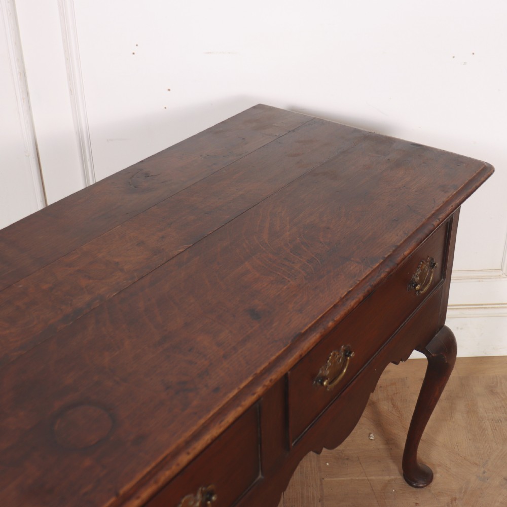 An 18th-century style dark oak dresser base featuring three frieze drawers, brass handles, a shaped apron, and elegant cabriole legs. View X