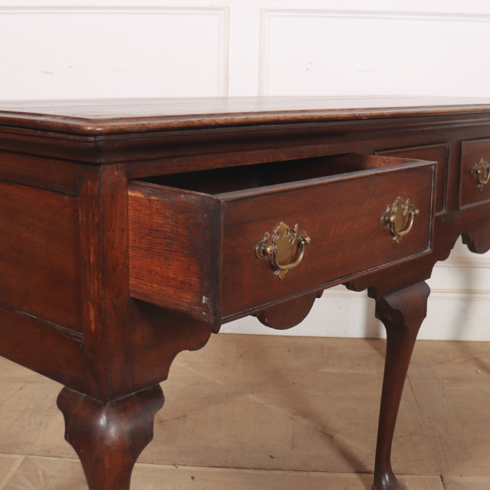An 18th-century style dark oak dresser base featuring three frieze drawers, brass handles, a shaped apron, and elegant cabriole legs. View XI
