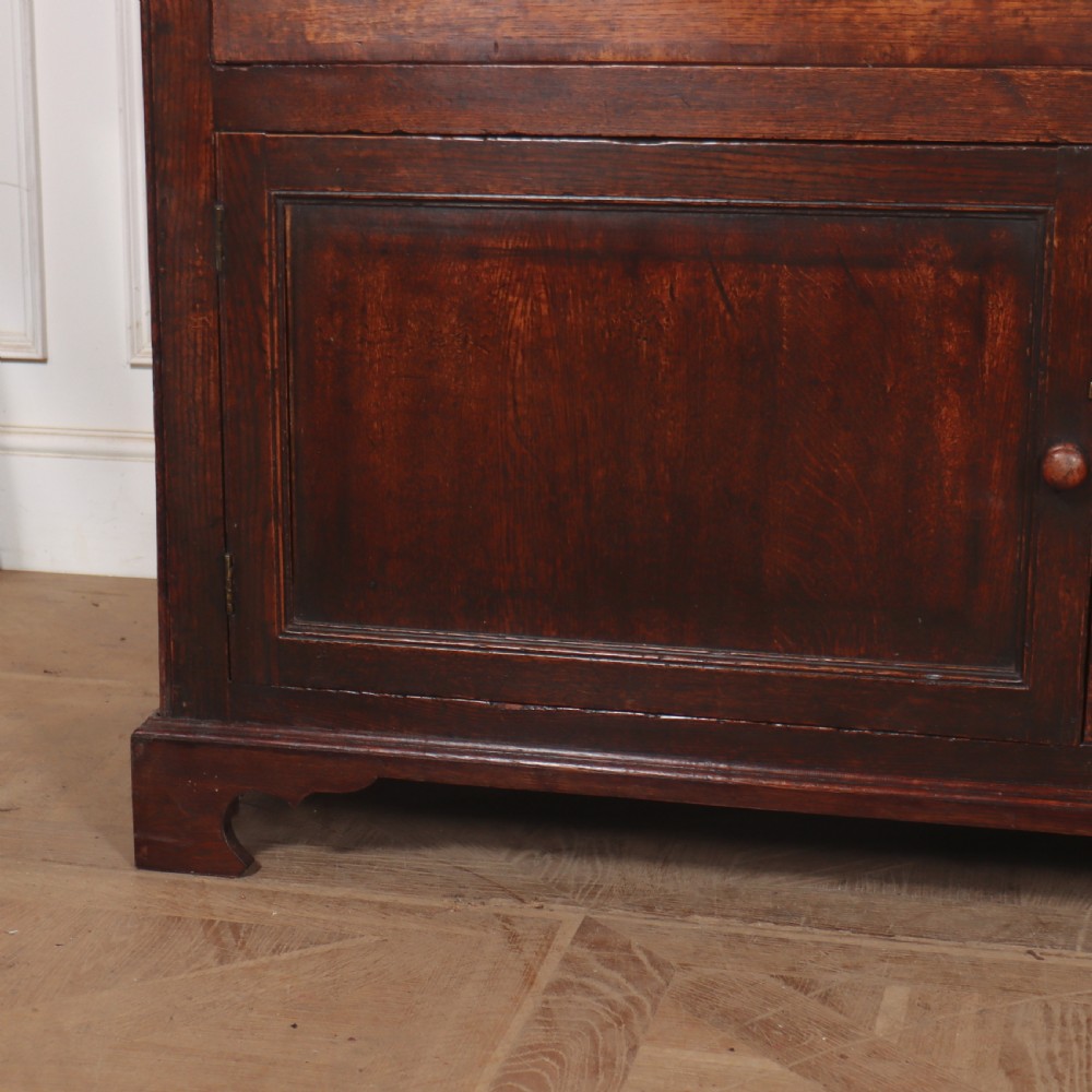 An antique English pine dresser base featuring four fielded cupboard doors with wooden knobs, keyhole escutcheons, fluted vertical details, and bracket feet. View II