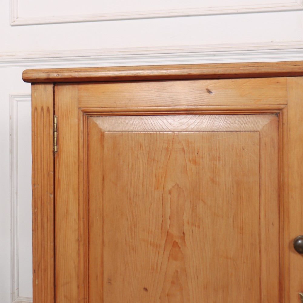 An antique English pine dresser base featuring four fielded cupboard doors with wooden knobs, keyhole escutcheons, fluted vertical details, and bracket feet. View III