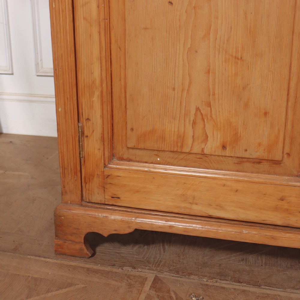 An antique English pine dresser base featuring four fielded cupboard doors with wooden knobs, keyhole escutcheons, fluted vertical details, and bracket feet. View IV