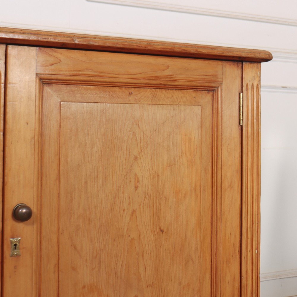 An antique English pine dresser base featuring four fielded cupboard doors with wooden knobs, keyhole escutcheons, fluted vertical details, and bracket feet. View V