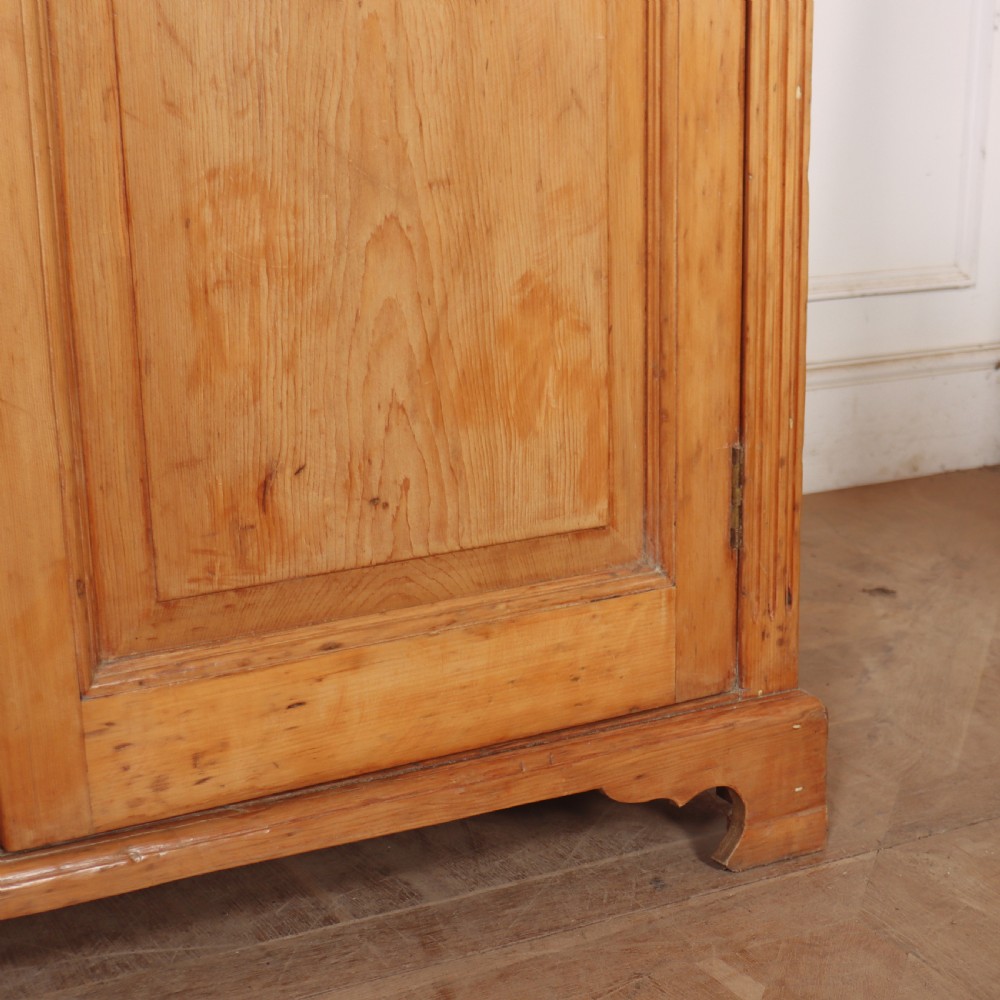 An antique English pine dresser base featuring four fielded cupboard doors with wooden knobs, keyhole escutcheons, fluted vertical details, and bracket feet. View VI