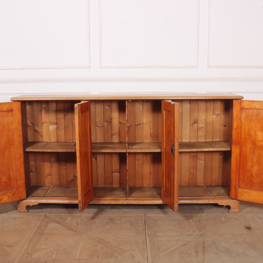 An antique English pine dresser base featuring four fielded cupboard doors with wooden knobs, keyhole escutcheons, fluted vertical details, and bracket feet. View VII