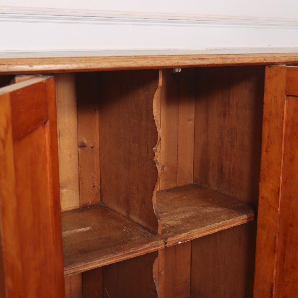 An antique English pine dresser base featuring four fielded cupboard doors with wooden knobs, keyhole escutcheons, fluted vertical details, and bracket feet. View VIII
