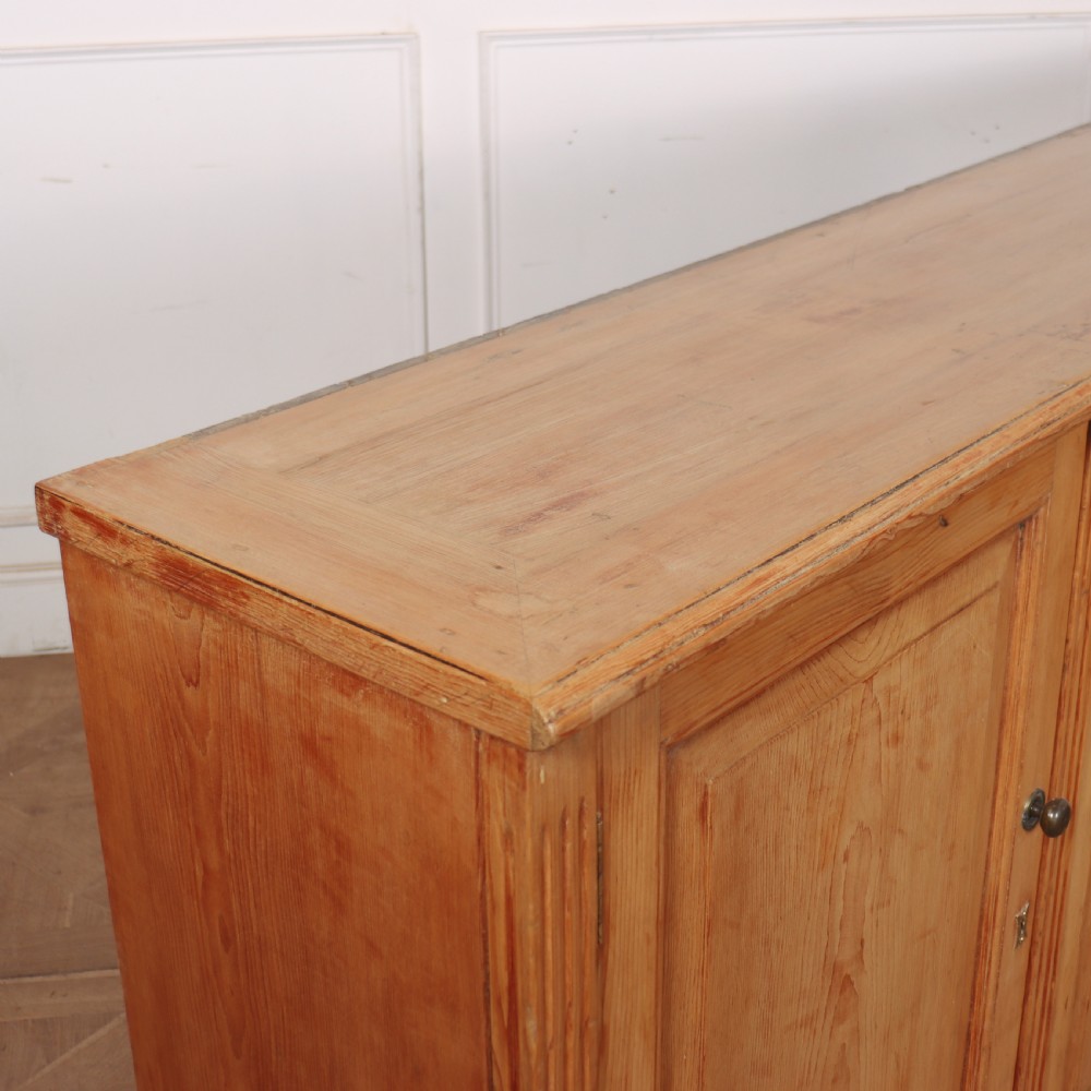 An antique English pine dresser base featuring four fielded cupboard doors with wooden knobs, keyhole escutcheons, fluted vertical details, and bracket feet. View IX