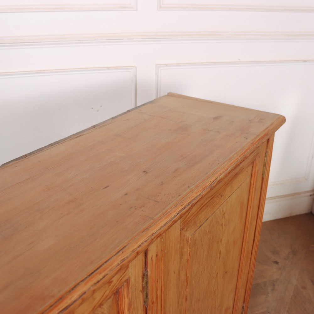 An antique English pine dresser base featuring four fielded cupboard doors with wooden knobs, keyhole escutcheons, fluted vertical details, and bracket feet. View X