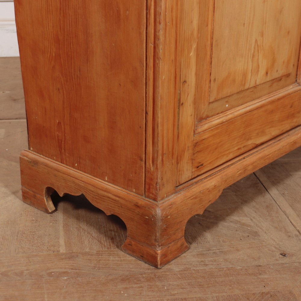 An antique English pine dresser base featuring four fielded cupboard doors with wooden knobs, keyhole escutcheons, fluted vertical details, and bracket feet. View XI