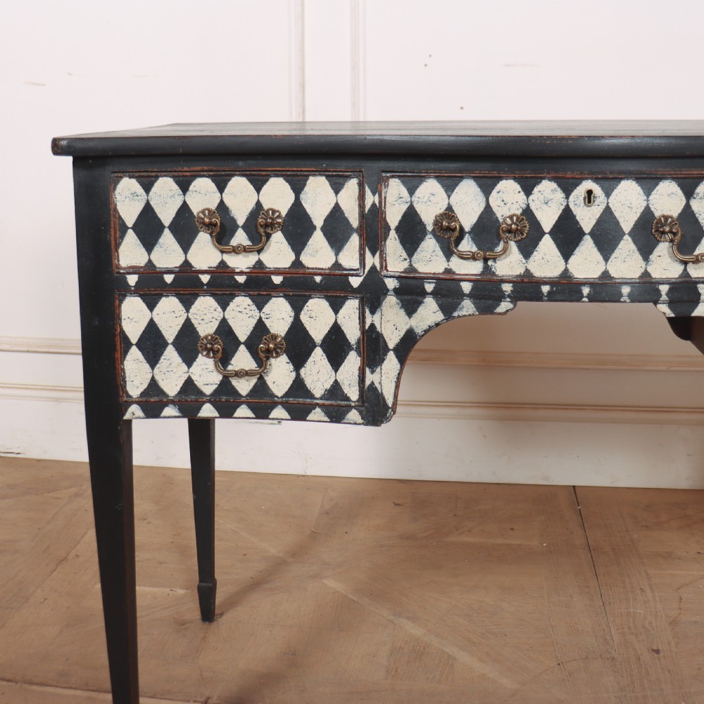 A black painted English serpentine desk featuring a cream and black harlequin pattern on five drawer fronts, brass drop handles, and tapered square legs. View II