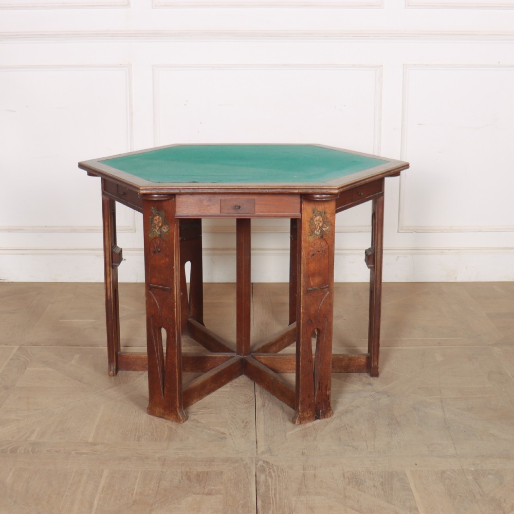 An antique hexagonal Arts and Crafts walnut card table featuring a green baize top, pierced leg details, and integrated drawers.