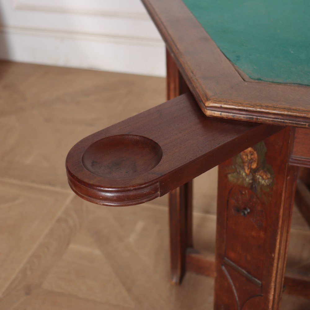 An antique hexagonal Arts and Crafts walnut card table featuring a green baize top, pierced leg details, and integrated drawers. View VI