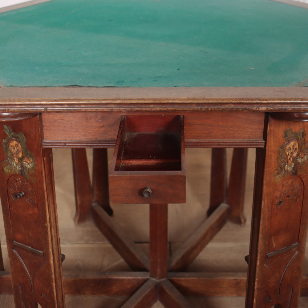 An antique hexagonal Arts and Crafts walnut card table featuring a green baize top, pierced leg details, and integrated drawers. View VII