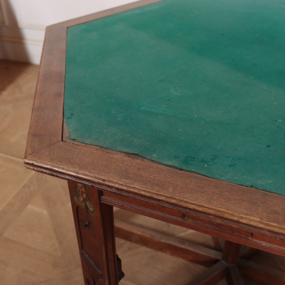 An antique hexagonal Arts and Crafts walnut card table featuring a green baize top, pierced leg details, and integrated drawers. View VIII