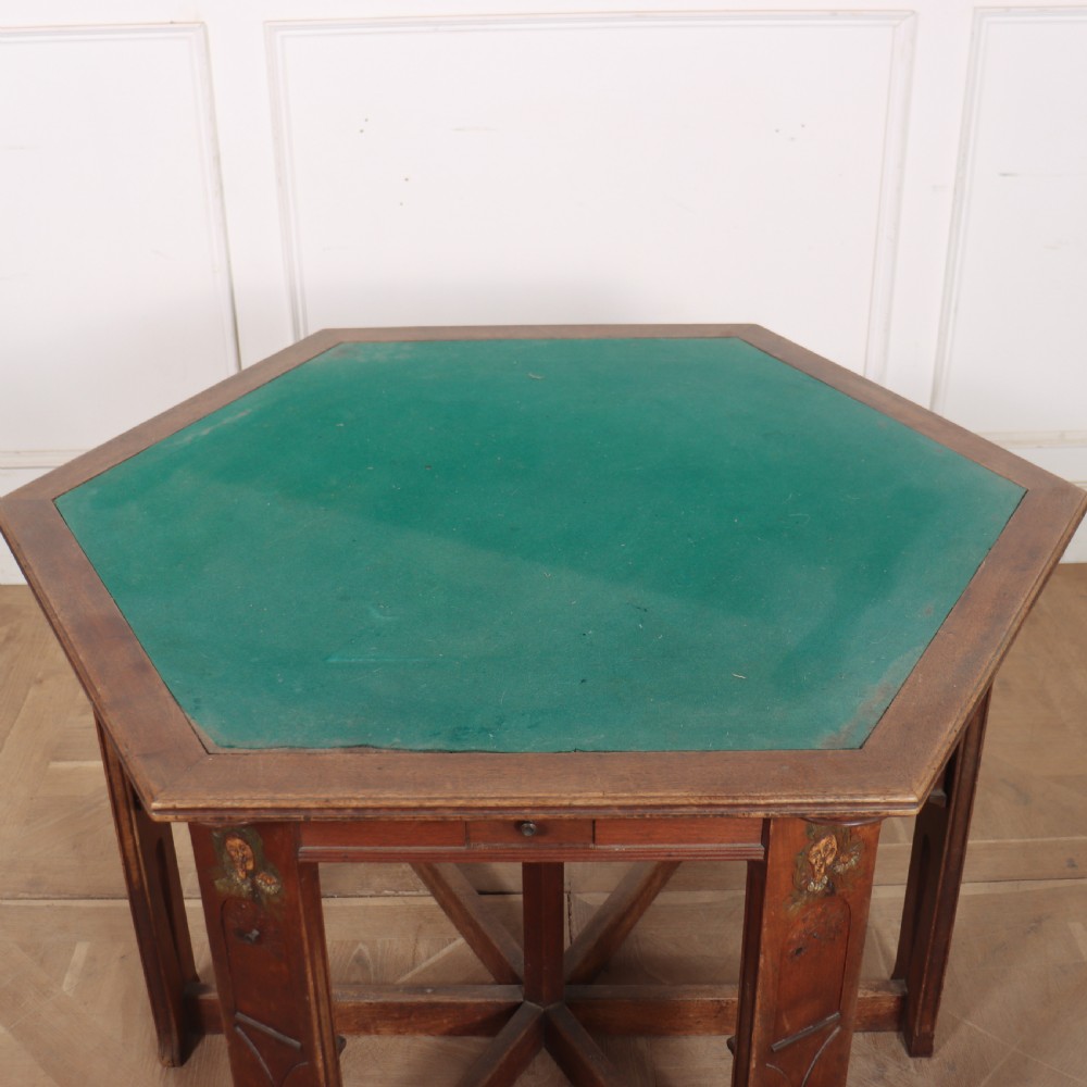 An antique hexagonal Arts and Crafts walnut card table featuring a green baize top, pierced leg details, and integrated drawers. View IX