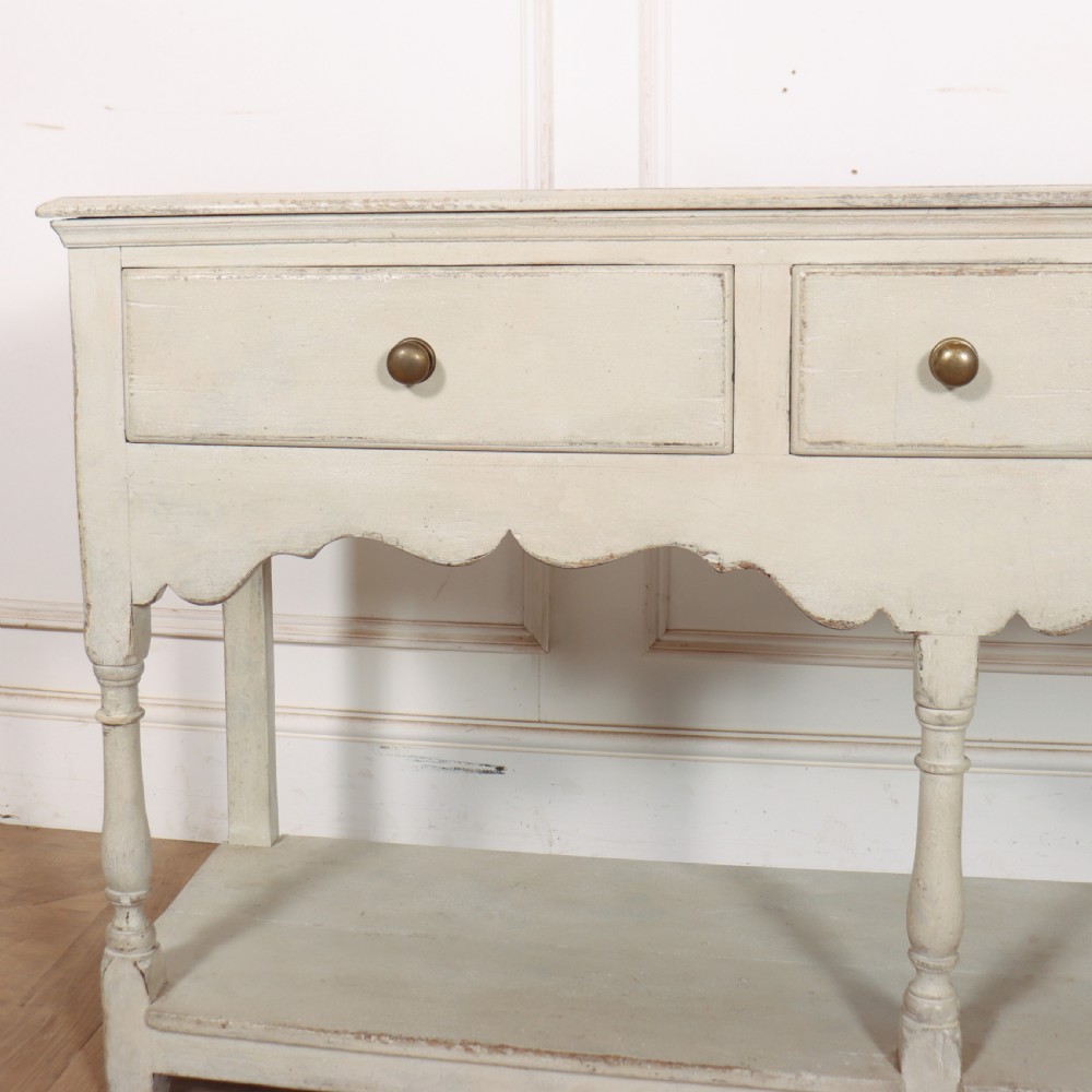 A painted cream timber potboard dresser base featuring three drawers with brass knobs, a scalloped apron, turned legs, and an open lower shelf. View II