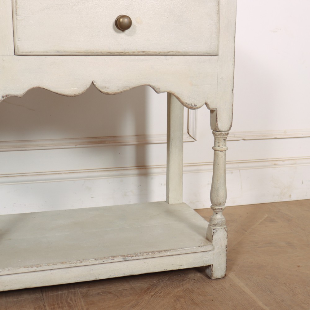 A painted cream timber potboard dresser base featuring three drawers with brass knobs, a scalloped apron, turned legs, and an open lower shelf. View VI