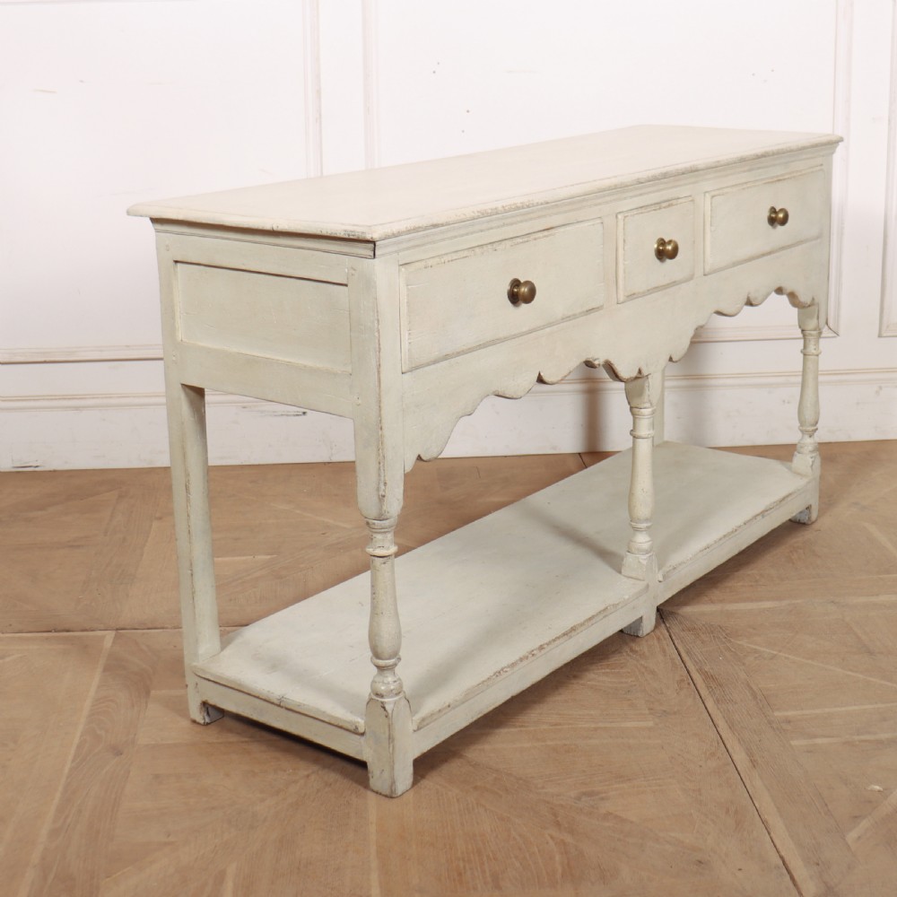 A painted cream timber potboard dresser base featuring three drawers with brass knobs, a scalloped apron, turned legs, and an open lower shelf. View VIII