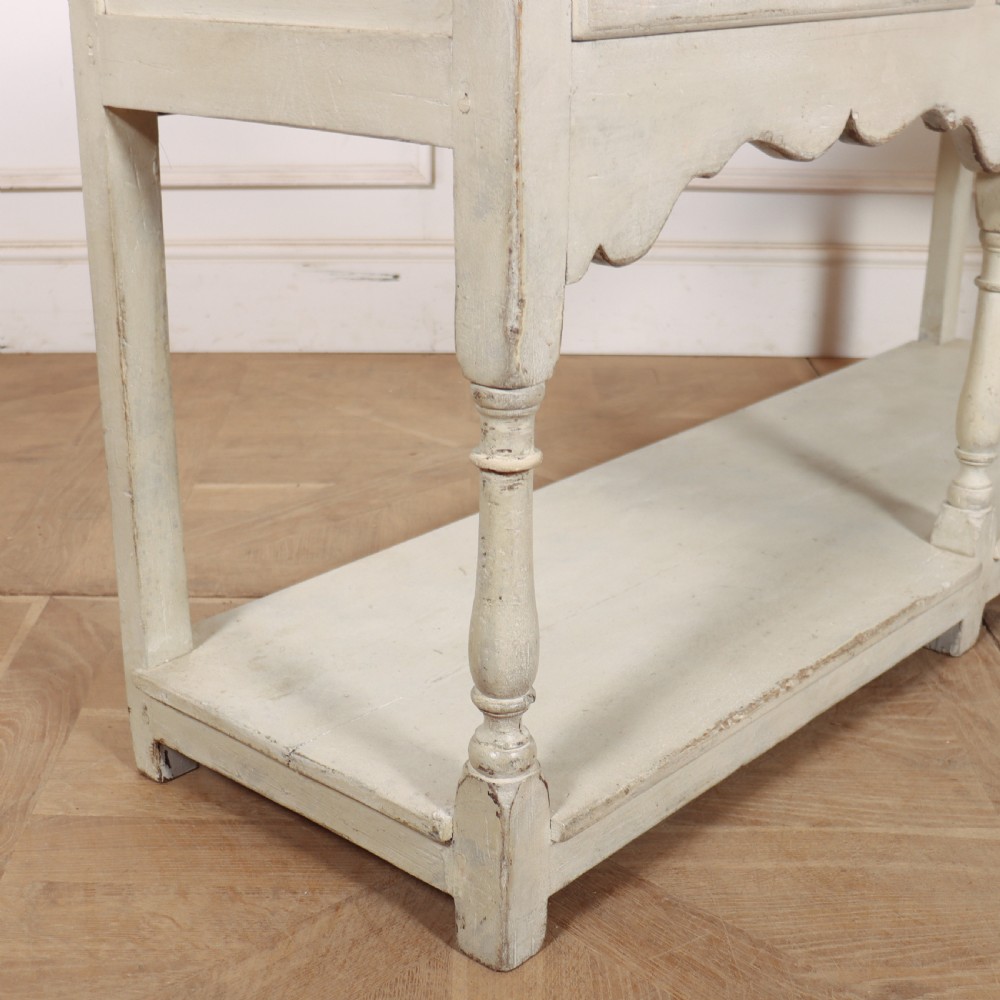 A painted cream timber potboard dresser base featuring three drawers with brass knobs, a scalloped apron, turned legs, and an open lower shelf. View IX