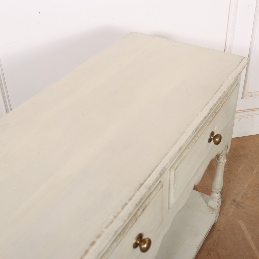 A painted cream timber potboard dresser base featuring three drawers with brass knobs, a scalloped apron, turned legs, and an open lower shelf. View XI