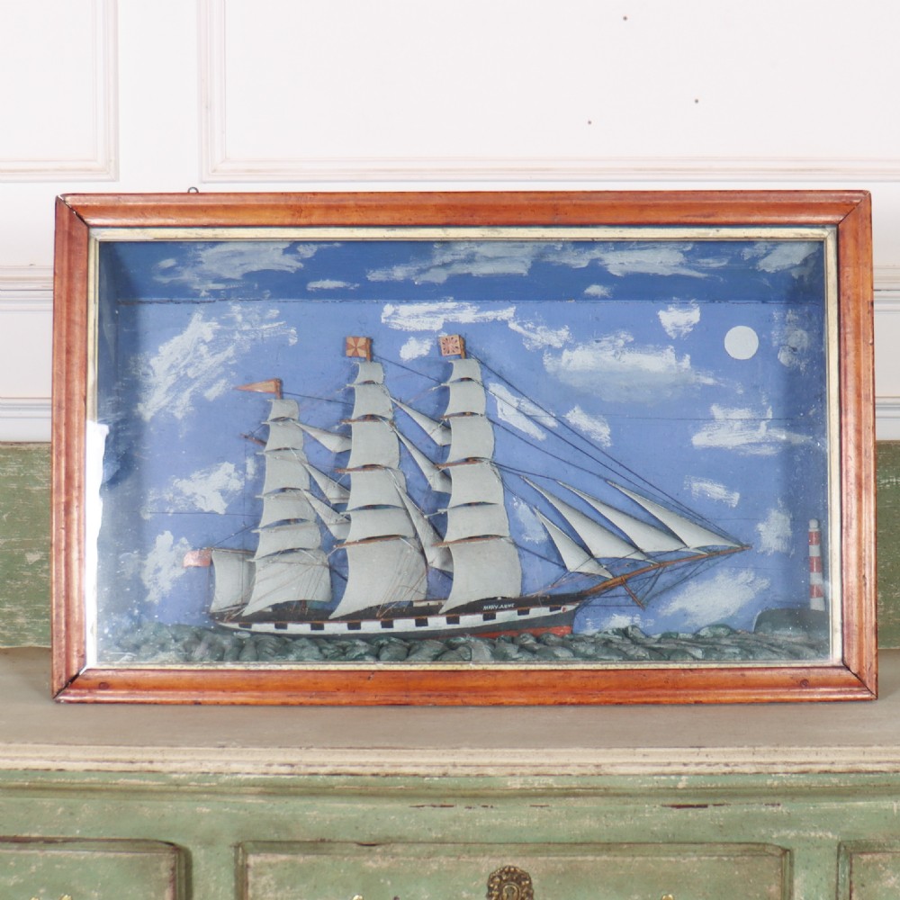 A framed glazed maritime diorama featuring a carved three-masted sailing vessel on a choppy painted sea set against a blue sky with a lighthouse.