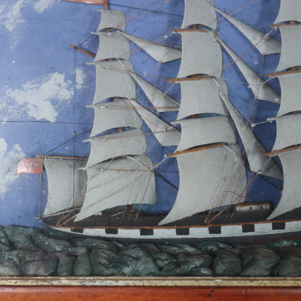 A framed glazed maritime diorama featuring a carved three-masted sailing vessel on a choppy painted sea set against a blue sky with a lighthouse. View IV