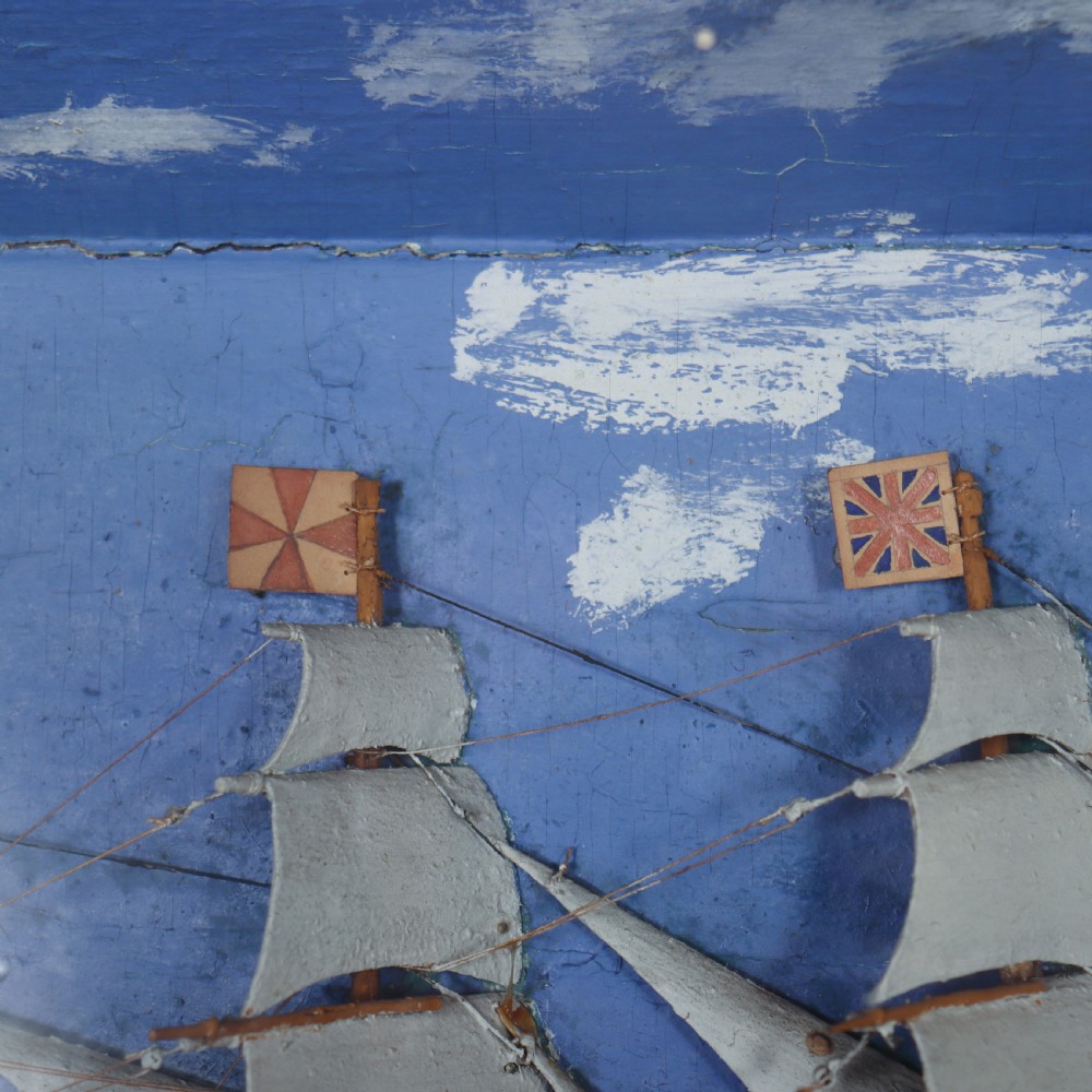 A framed glazed maritime diorama featuring a carved three-masted sailing vessel on a choppy painted sea set against a blue sky with a lighthouse. View V