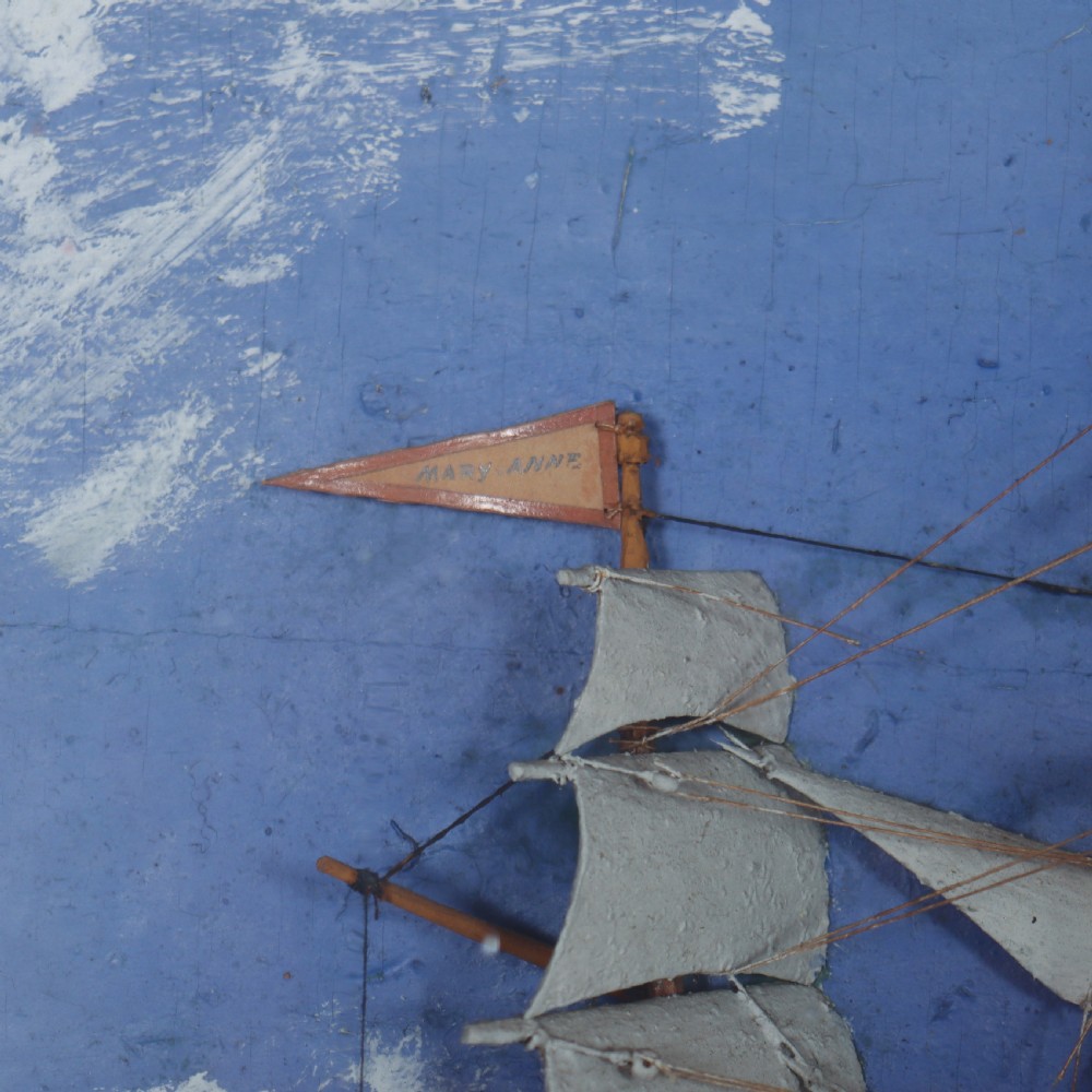 A framed glazed maritime diorama featuring a carved three-masted sailing vessel on a choppy painted sea set against a blue sky with a lighthouse. View VI
