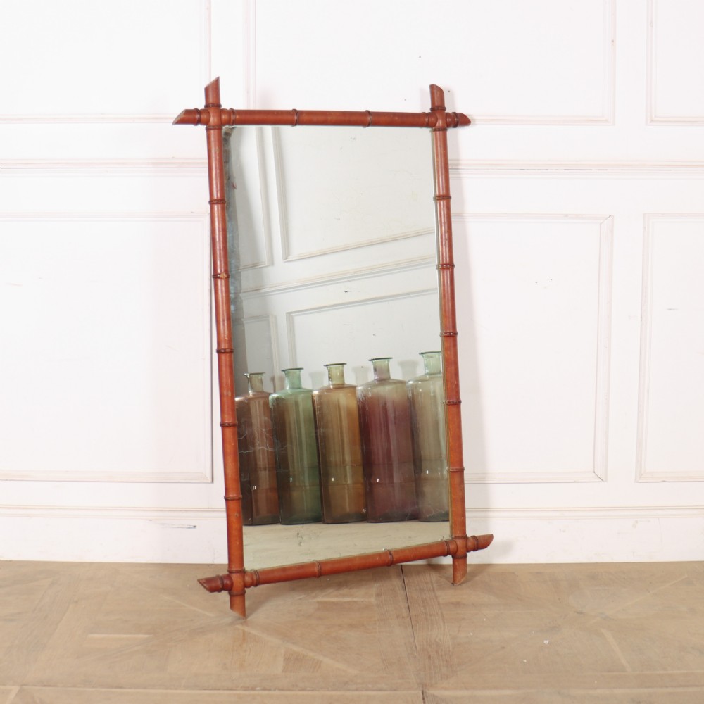 A large rectangular mirror framed in warm brown turned wood designed to mimic bamboo with extending corner joints.