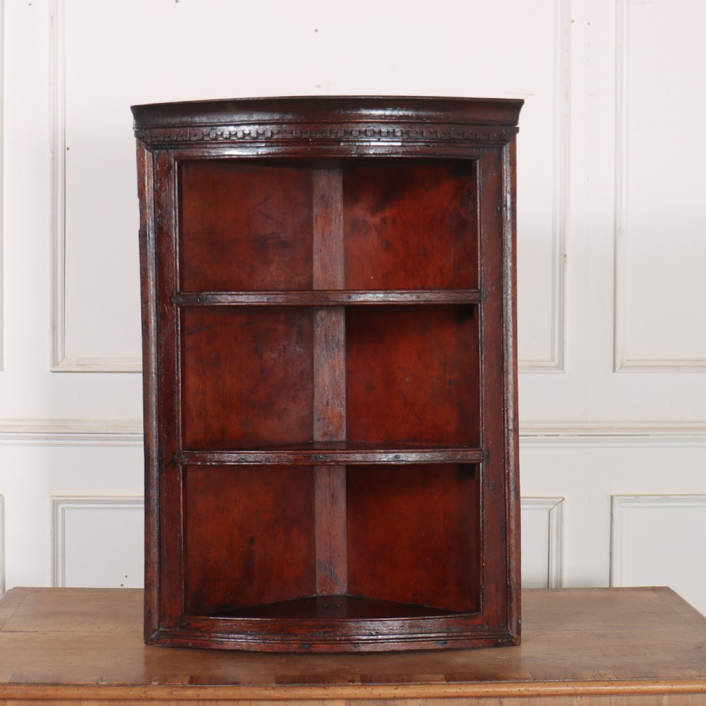 An 18th-century English dark wood hanging corner cupboard with three open curved shelves and moulded cornice.