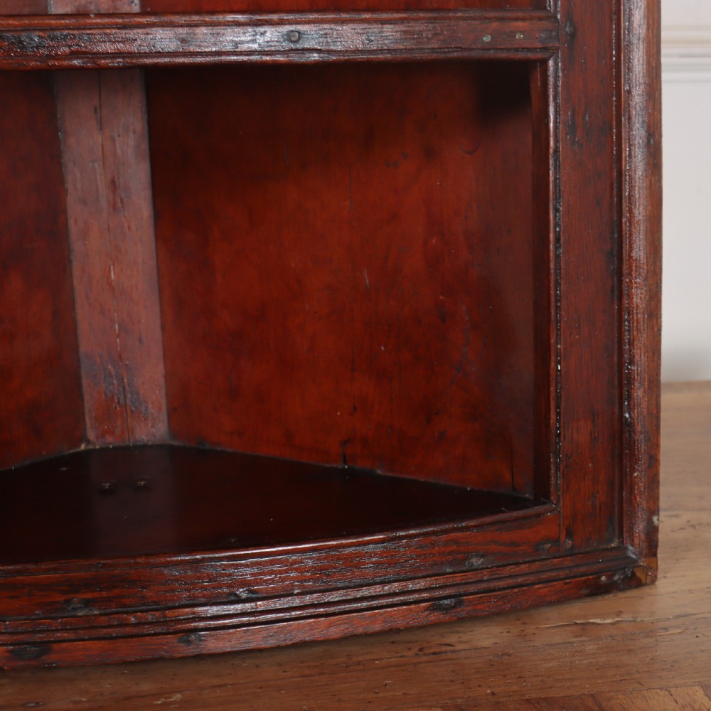 An 18th-century English dark wood hanging corner cupboard with three open curved shelves and moulded cornice. View V