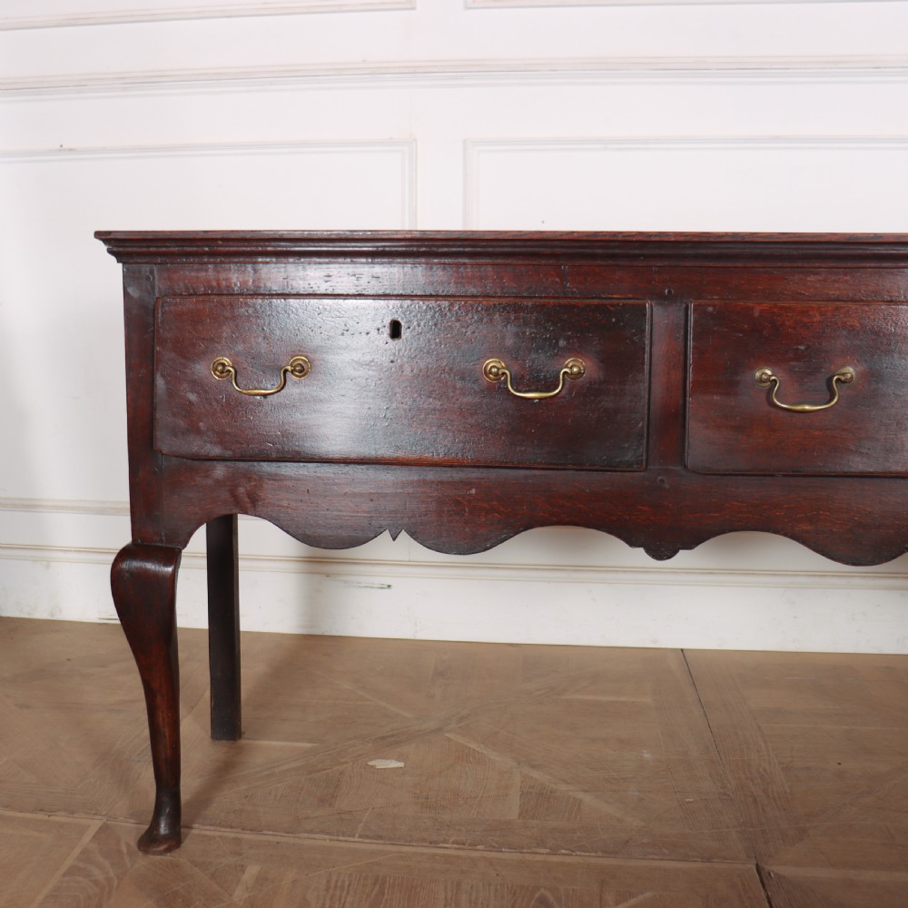 An 18th-century English oak dresser base featuring three drawers with brass handles, a scalloped apron, and cabriole legs. View II