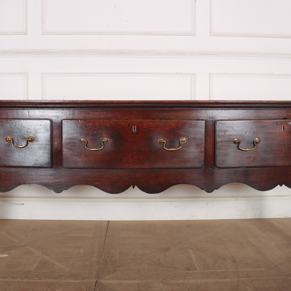 An 18th-century English oak dresser base featuring three drawers with brass handles, a scalloped apron, and cabriole legs. View III