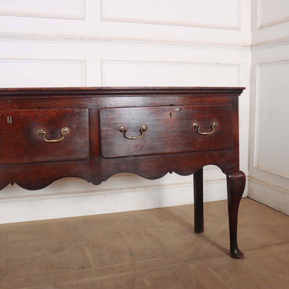 An 18th-century English oak dresser base featuring three drawers with brass handles, a scalloped apron, and cabriole legs. View V
