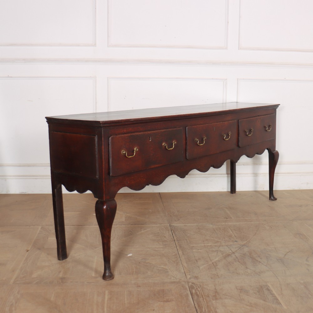 An 18th-century English oak dresser base featuring three drawers with brass handles, a scalloped apron, and cabriole legs. View VI