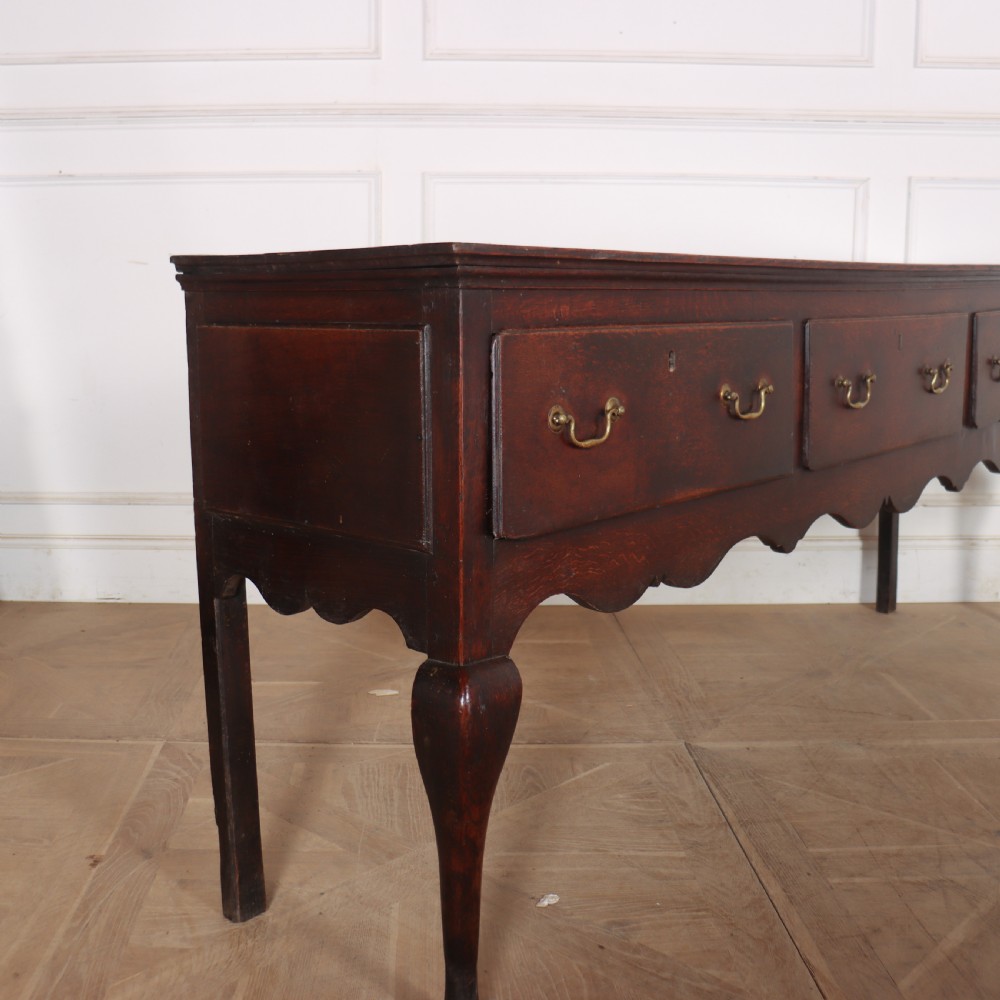 An 18th-century English oak dresser base featuring three drawers with brass handles, a scalloped apron, and cabriole legs. View VII